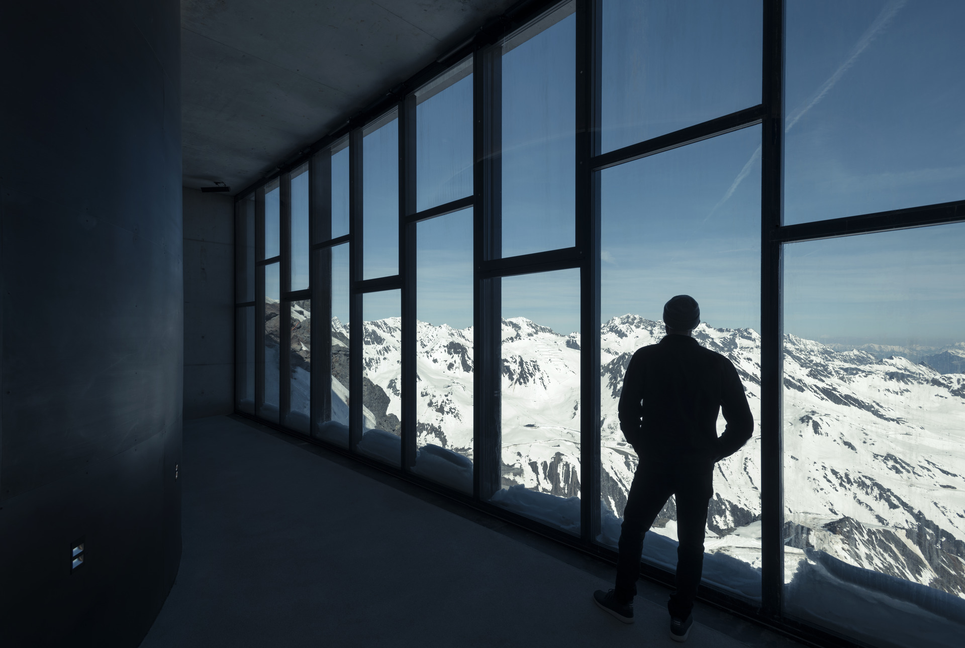 Shape of a man standing in front of large windows overlooking snowy mountaintops