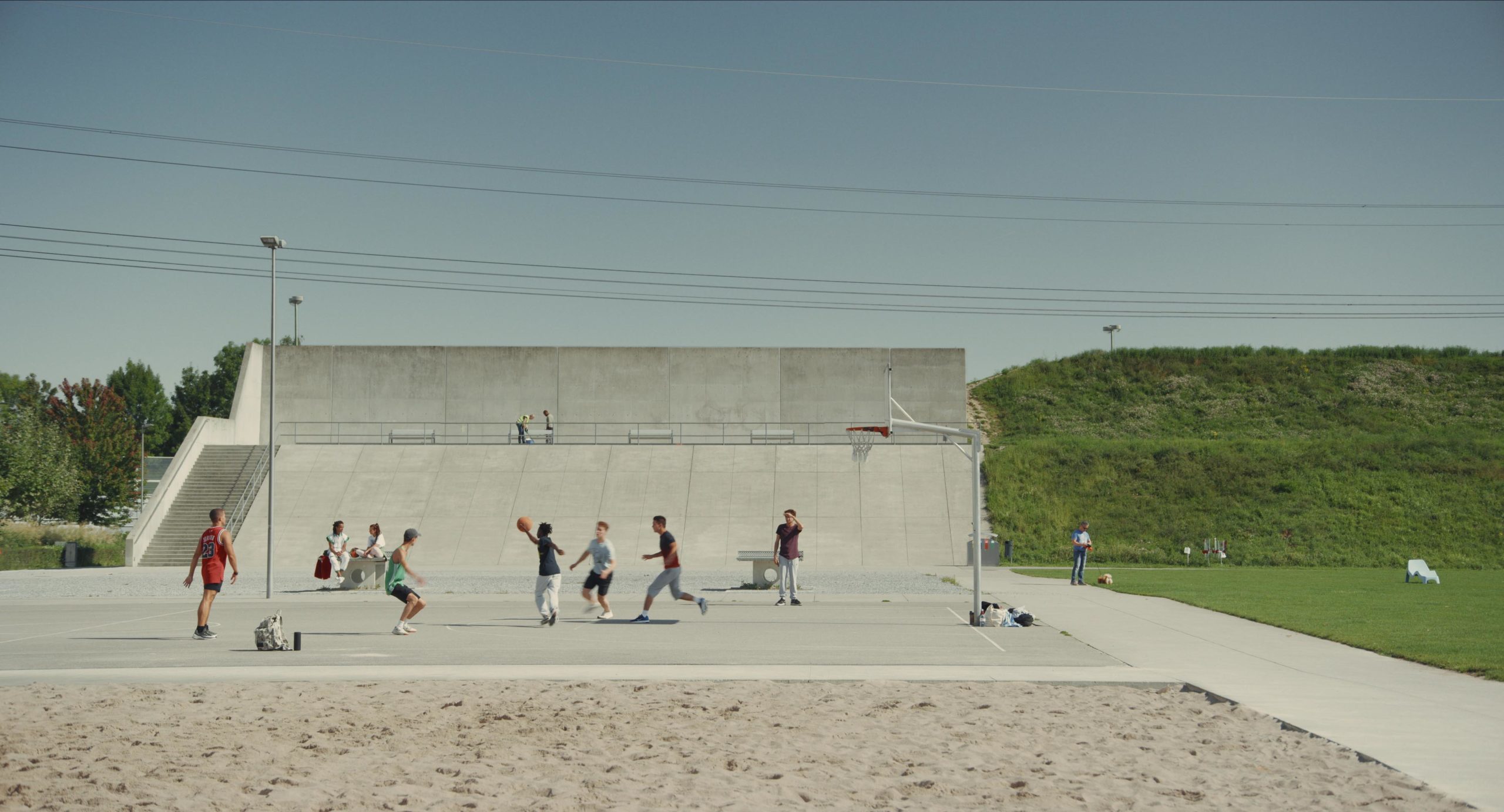 Young people playing basketball in front of concrete steps, next to a lawn