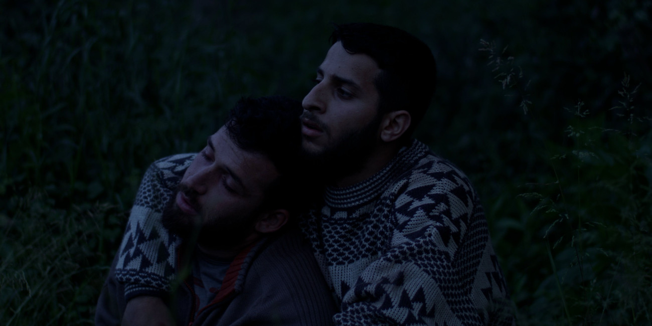 photo of two beraded man in dark forest, one has his arms around the other