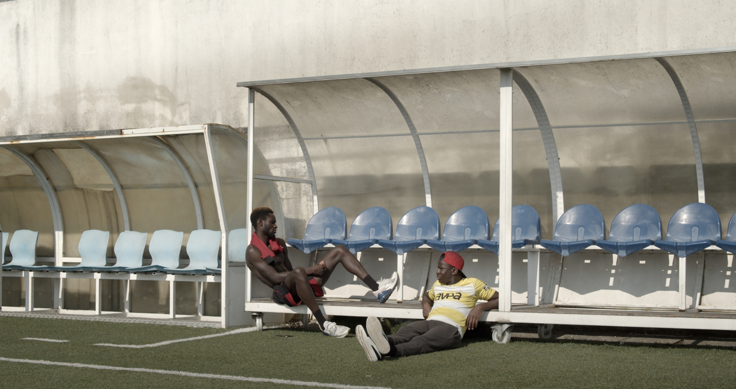 still of two black footballers reposing at coach's bench