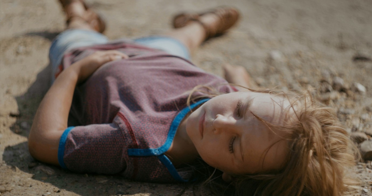 still of a child lying on sandy ground
