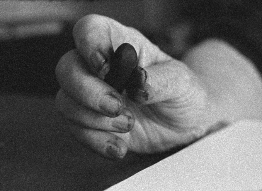 B&W still of a hand holding a piece of drawing chalk