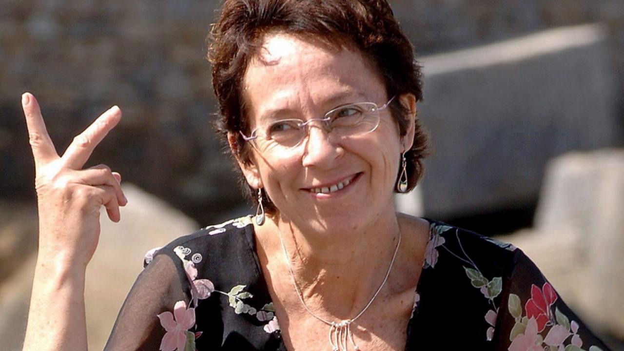 Photo of a bespectacled person holding up her hand in a 