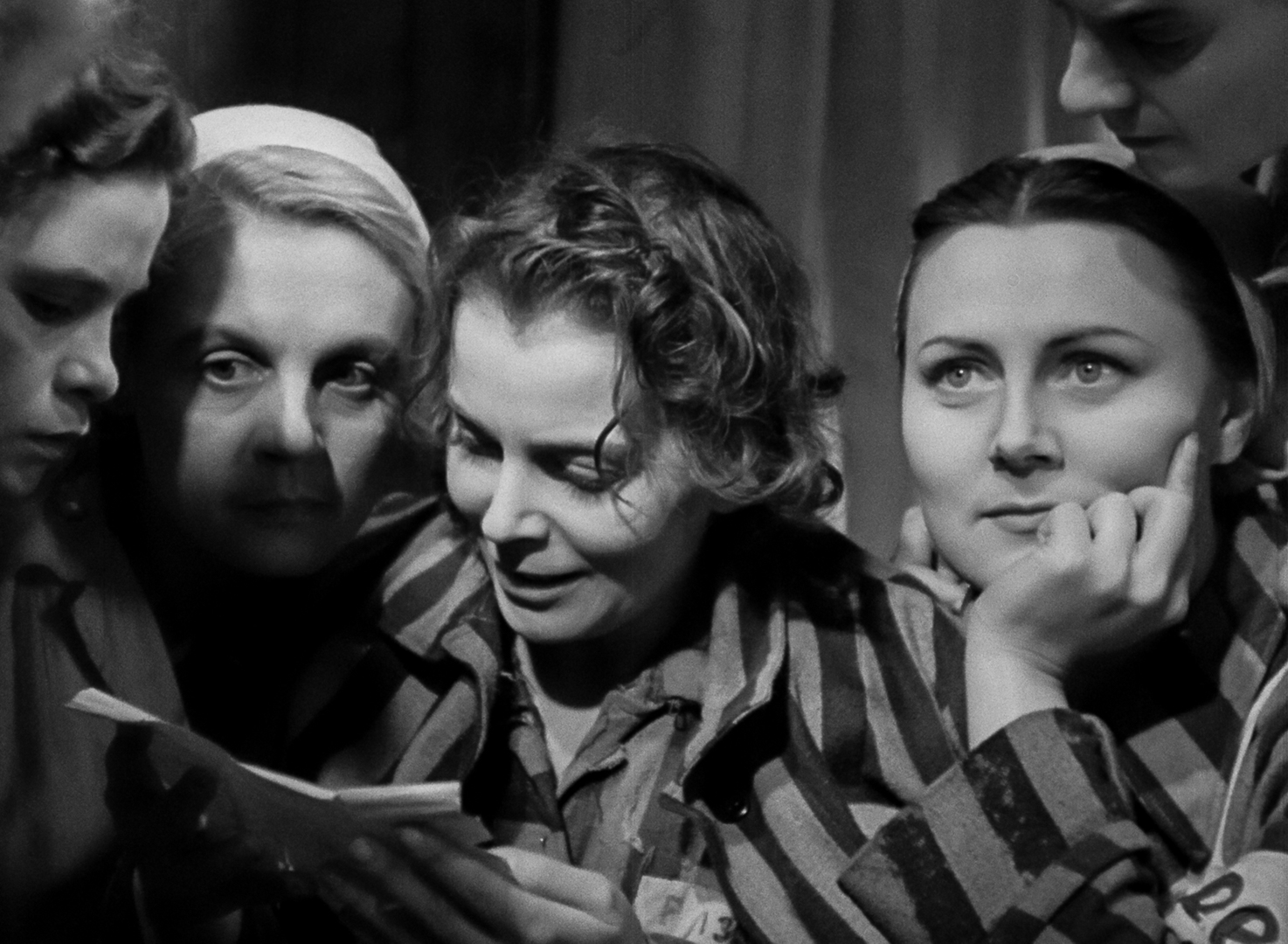 Film still: Four female concentration camp inmates, one of them reading from a letter